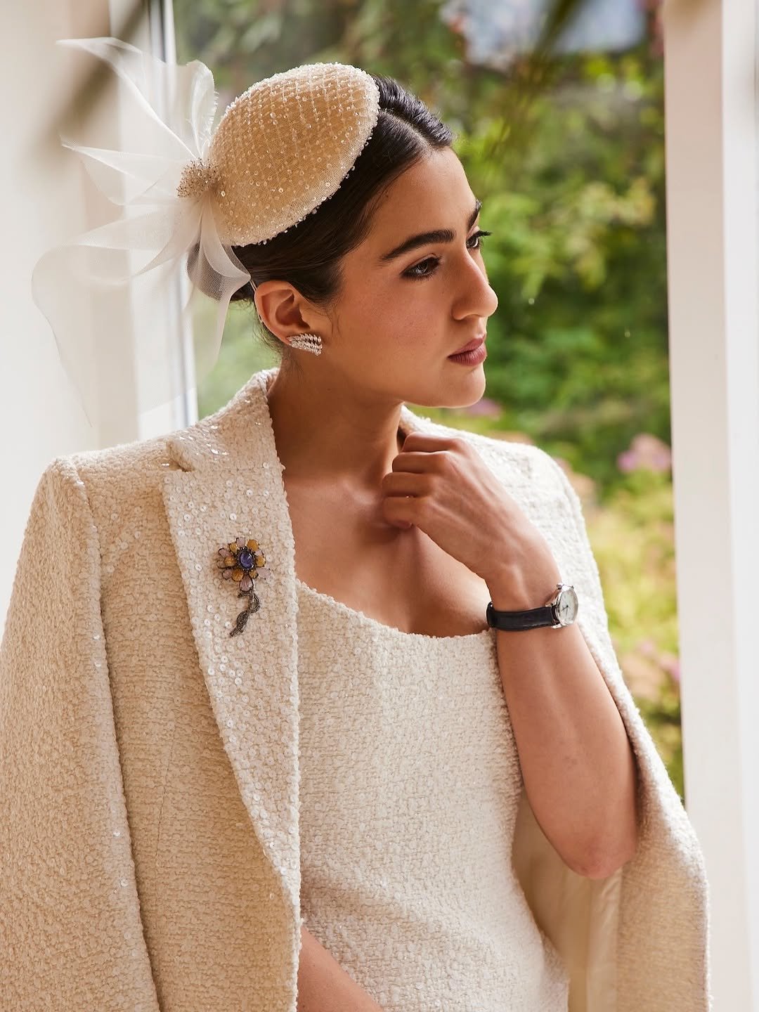 Sara Ali Khan জানালার পাশে দাঁড়িয়ে ivory টুইড কেপ ও fascinator পরে, হাতে Longines ঘড়ি