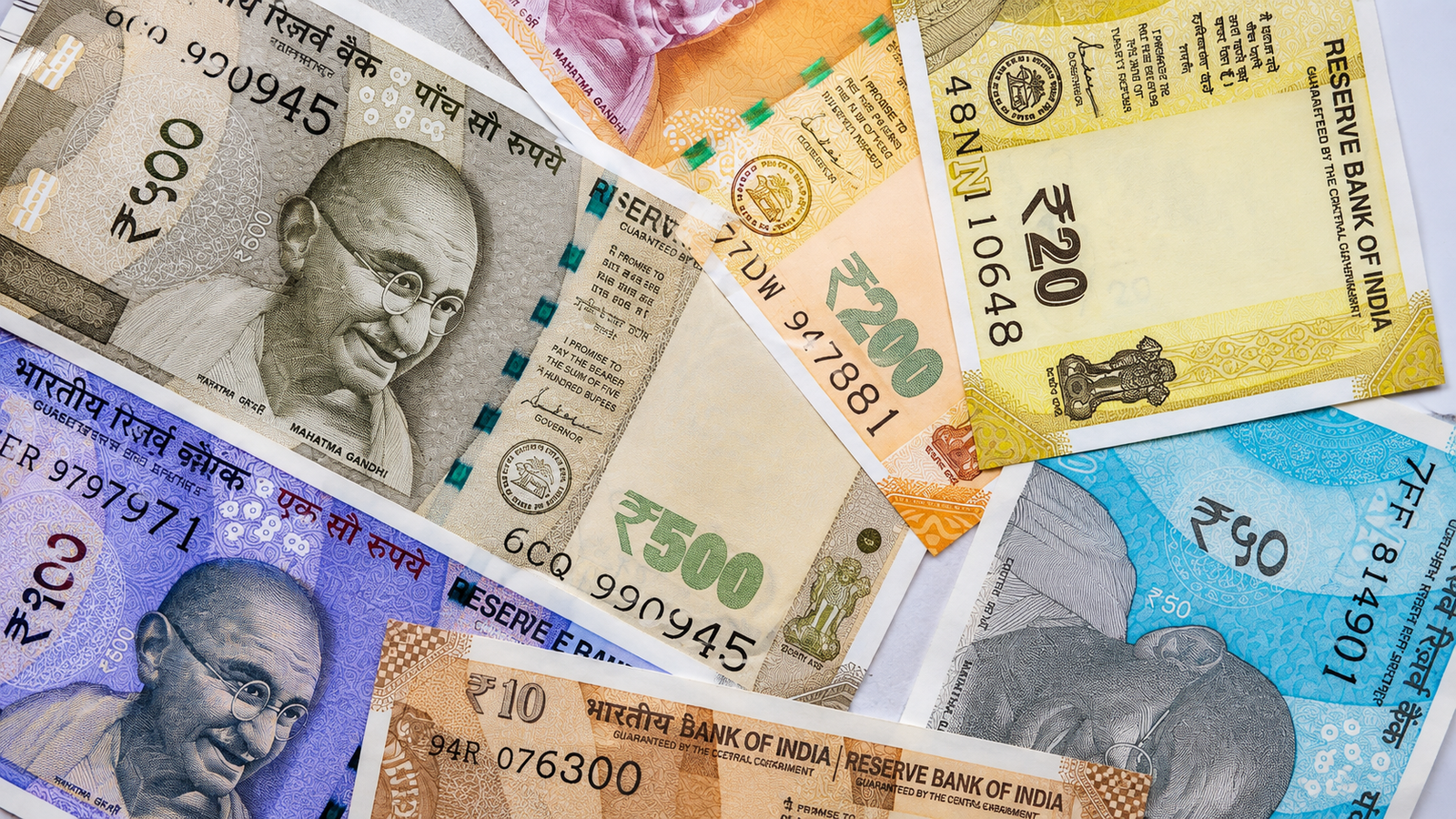 RBI Repo Rate অপরিবর্তিত রাখল, বৃদ্ধির হার বাড়িয়ে মুদ্রাস্ফীতির পূর্বাভাস কমাল কেন্দ্রীয় ব্যাংক Reserve Bank of India RBI ভবনের সামনে repo rate ঘোষণা সংক্রান্ত ব্যানার, ভারতীয় বিভিন্ন মূল্যের রুপির নোটের ক্লোজ আপ ছবি। ছবিতে ২০, ৫০, ১০০, ২০০ ও ৫০০ টাকার নোট একসঙ্গে সাজানো রয়েছে, যা ভারতের মুদ্রা ব্যবস্থা ও নগদ অর্থ লেনদেনকে তুলে ধরছে।